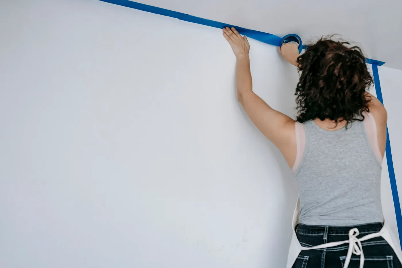 Masking tape being laid along a ceiling line before painting